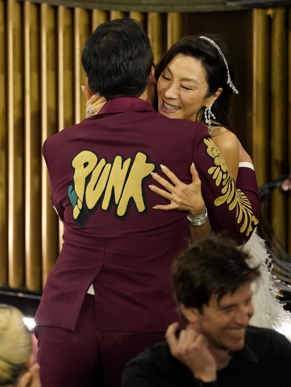 Daniel Kwan, left, is hugged in the audience by Michelle Yeoh as he accepts the award for best original screenplay for "Everything Everywhere All at Once" at the Oscars on Sunday, March 12, 2023, at the Dolby Theatre in Los Angeles. (AP Photo/Chris Pizzello)