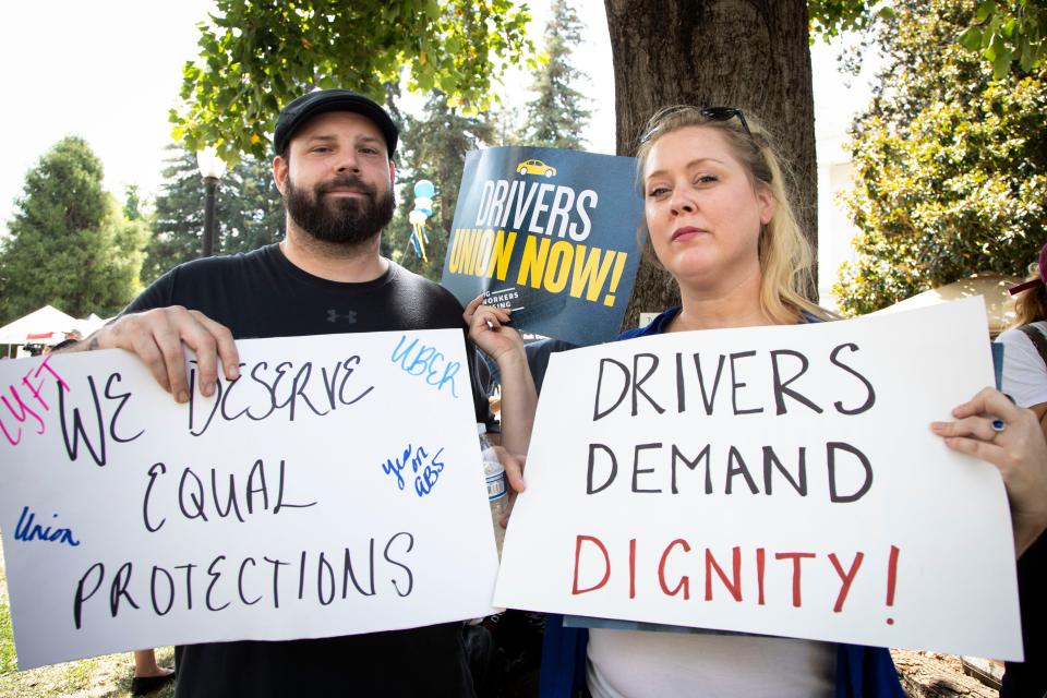 Lyft drivers Erica Mighetto and Danny Raviart hold signs in support of AB 5 on Wednesday, Aug. 28, 2019, in  Sacramento, Calif.
