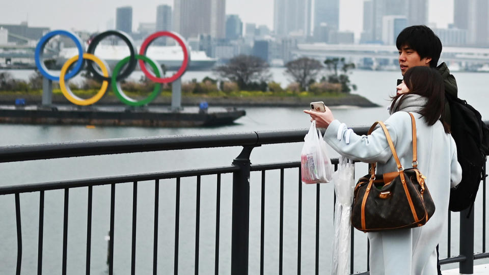 The Olympic rings in the background after as people look on.