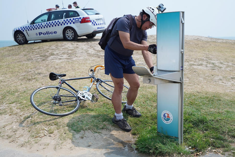 A cyclist fills up his water bottle while police watch over the public cooling down on St Kilda beach during hot weather in Melbourne.