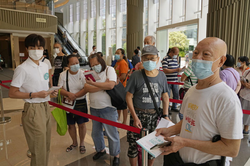 In this Tuesday, June 15, 2021 photo, people wearing face masks to help prevent the spread of the coronavirus, line up to register for a coronavirus vaccine lottery in a Grand Central residential building complex in Hong Kong. Coronavirus vaccine incentives offered by Hong Kong companies, including a lucky draw for an apartment, a Tesla car and even gold bars, are helping boost the city’s sluggish inoculation rate. (AP Photo/Kin Cheung)