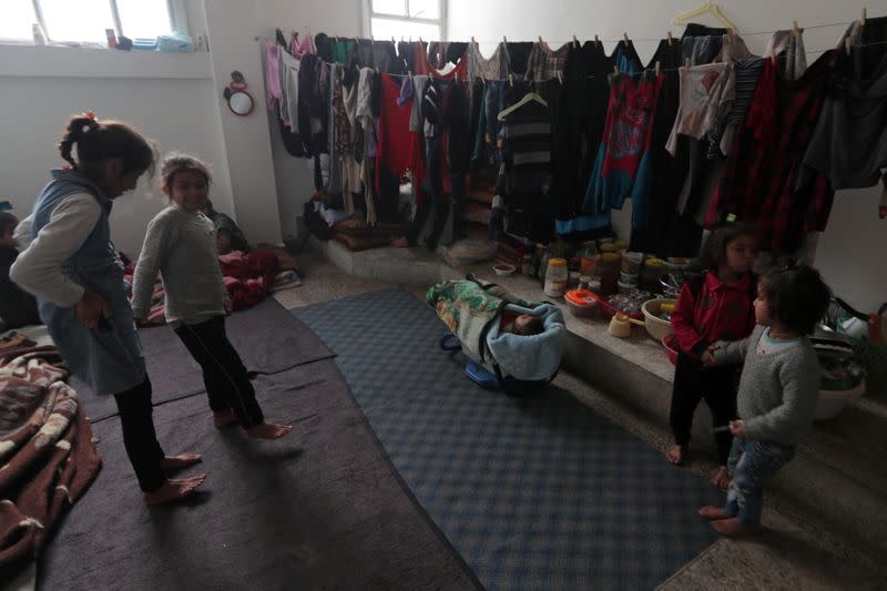 Internally displaced children stand near hanging clothes inside a room in Azaz