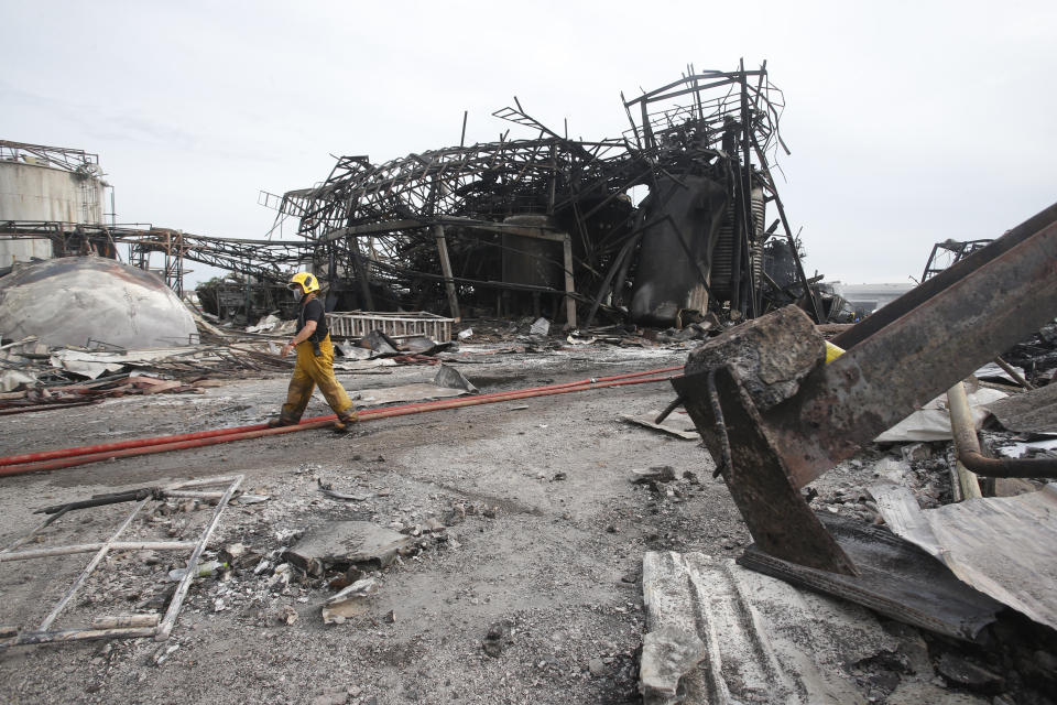 A firefighter walks in front of twisted metal frames of a charred chemical factory Tuesday, July 6, 2021, in Samut Prakan, Thailand. Firefighters finally extinguished a blaze at a chemical factory just outside the Thai capital early Tuesday, more than 24-hours after it started with an explosion that damaged nearby homes and then let off a clouds of toxic smoke that prompted a widespread evacuation. (AP Photo/Anuthep Cheysakron)
