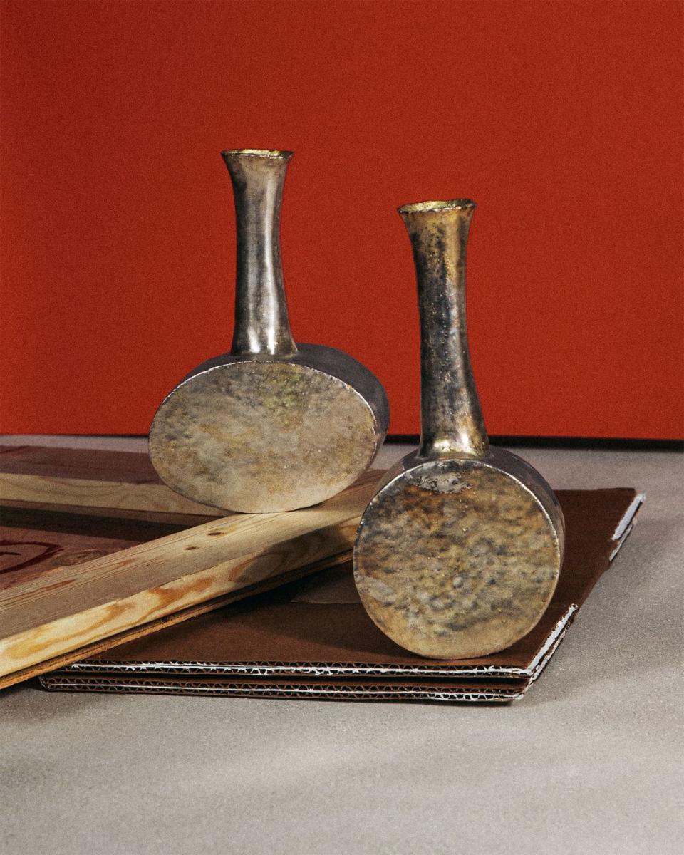 two small antique looking metal vases against a red background