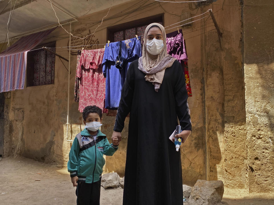 This April 17, 2020 photo, shows Sally Ahmed, a close friend of 73-year-old Ghaliya Abdel-Wahab who died from COVID-19 on April 6, 2020, standing with her son on one of two streets on complete lockdown closed off by security forces for people to quarantine after her death, in Bahtim, Shubra el-Kheima neighborhood, Qalyoubiya governorate, Egypt. (AP Photo/Nariman El-Mofty)