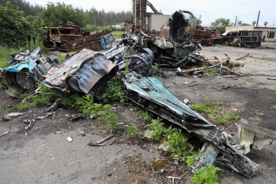 The twisted metal wreckage of a fighter jet, surrounded by other twisted metal near some woodland.