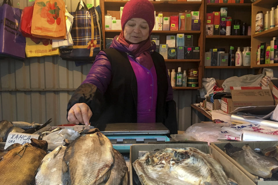 Irina Vakulina, 58, who used to live on the other side but switched to Russian citizenship in the early 2000s because she and her husband found a nicer house there, sells smoked fish and foreign-made perfume in a kiosk in Chertkovo, Russia, Sunday, Dec. 2, 2018. On the map Chertkovo and Milove is one village, which is crossed by the main road called Friendship of People's Street. People on the streets easily mix both Russia and Ukrainian languages without making a political statement of it, but earlier this year, Russia built a barbed wire fence on the Friendship of People's street, marking the border with Ukraine in a metaphorical statement about the long-simmering conflict between the countries. (AP Photo/Nataliya Vasilyeva)