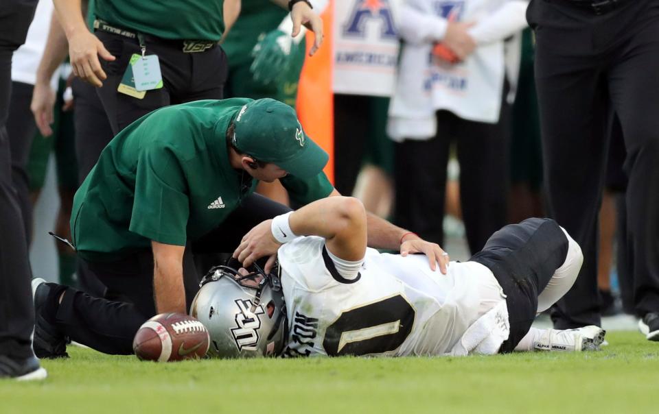 A trainer from South Florida attends to Central Florida quarterback McKenzie Milton after he went down with an apparent knee injury during the first half of an NCAA college football game Friday, Nov. 23, 2018, in Tampa, Fla. (AP Photo/Mike Carlson)