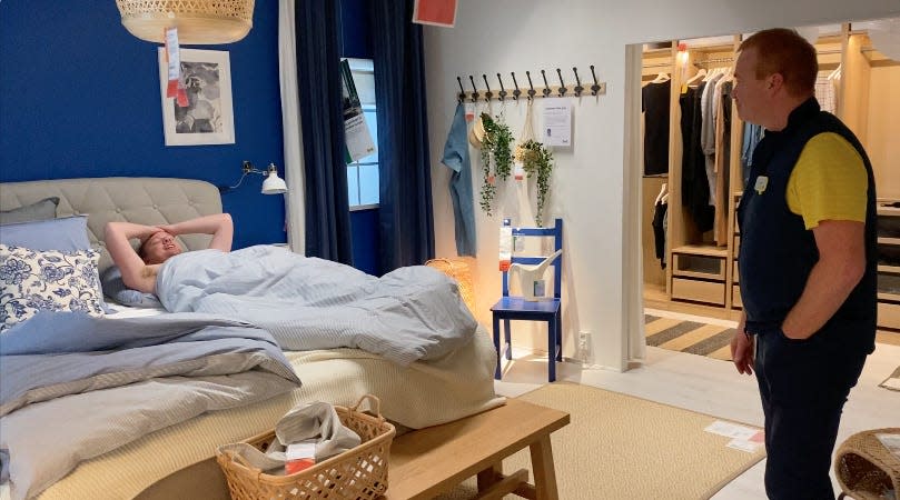 A man lies in an IKEA showroom bed in Aalborg, Denmark (L) as store manager Peter Elmose looks on (R).