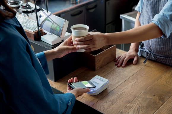 A person paying for cup of coffee using Apple Pay on a smartphone.