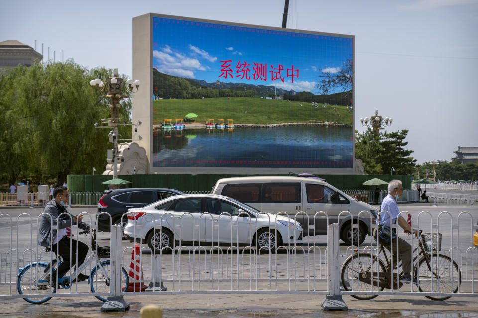 People ride bicycles past a large video screen with the words "System in Testing" set up near Tiananmen Square in Beijing, Tuesday, June 22, 2021. Chinese authorities have closed Beijing's central Tiananmen Square to the public, eight days ahead of a major celebration being planned to mark the 100th anniversary of the founding of the ruling Communist Party. (AP Photo/Mark Schiefelbein)