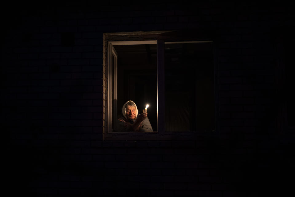 Catherine, 70, looks out the window while holding a candle for light inside her house during a power outage, in Borodyanka, Kyiv region, Ukraine, Thursday, Oct. 20, 2022. Airstrikes cut power and water supplies to hundreds of thousands of Ukrainians on Tuesday, part of what the country's president called an expanding Russian campaign to drive the nation into the cold and dark and make peace talks impossible. (AP Photo/Emilio Morenatti)