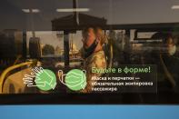 A woman is seen through a glass window with the words reading "Keep fit! Mask and gloves are compulsory equipment of passengers" inside a bus in Moscow, Russia, Tuesday, June 22, 2021. An ambitious plan of vaccinating 30 million Russians by mid-June against the coronavirus has fallen short by a third, and the country has started to see a surge in daily new infections. So now, many regional governments across the vast country are obligating some workers to get vaccinated and requiring the shots to enter certain businesses, like restaurants. (AP Photo/Pavel Golovkin)