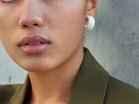 woman wearing a green monochrome outfit, statement eyeliner, and simple silver jewelry sitting up against a wall