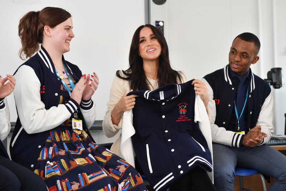 The Duchess of Sussex is presented with an item of school clothing as she joins in a discussion of the 'Senior Debate Squad' at the Robert Clack Upper School in Dagenham, Essex, during a surprise visit to celebrate International Women's Day.