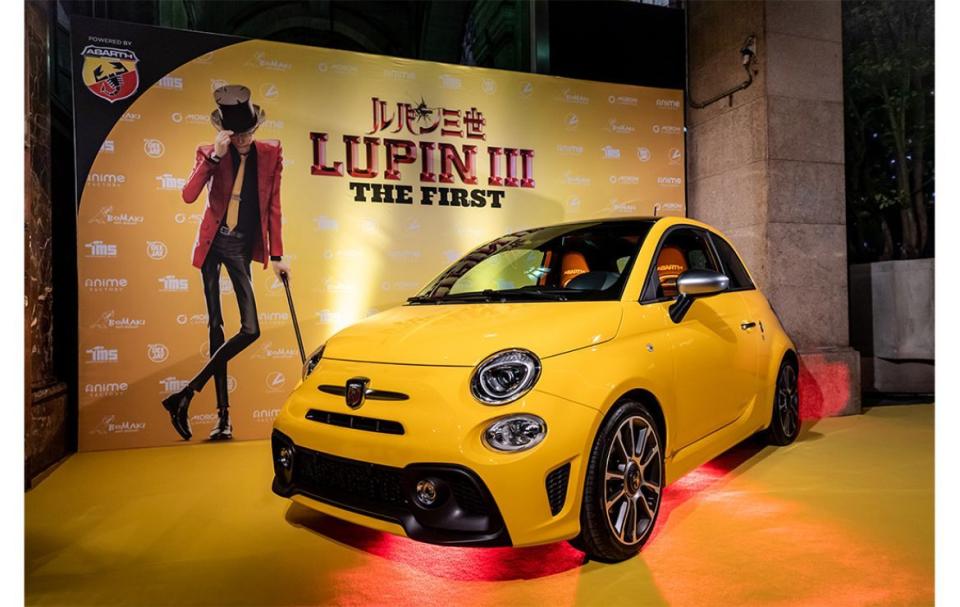 yellow fiat parked in front of lupin poster