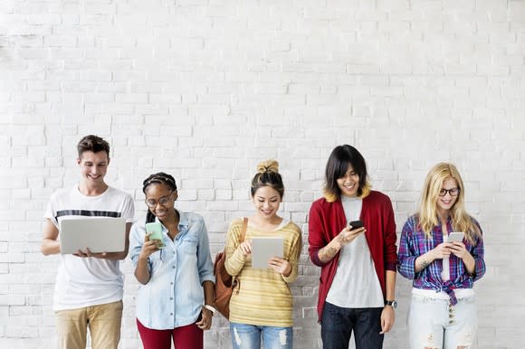 Five smiling young people using mobile devices.