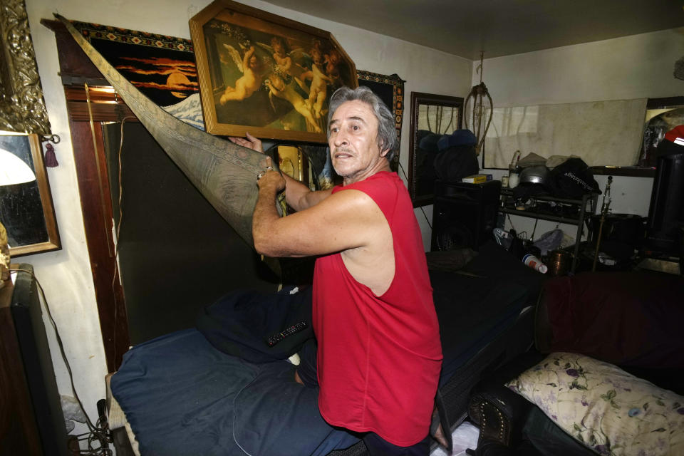 Ben Gallegos pulls back a covering to show the foam pad used to insulate a window in his family's home in the Globeville neighborhood as the daytime high temperature soars toward triple digits, Thursday, July 27, 2023, in north Denver. Gallegos has taken several measures to keep his home cool in spite of lacking central air conditioning. (AP Photo/David Zalubowski)