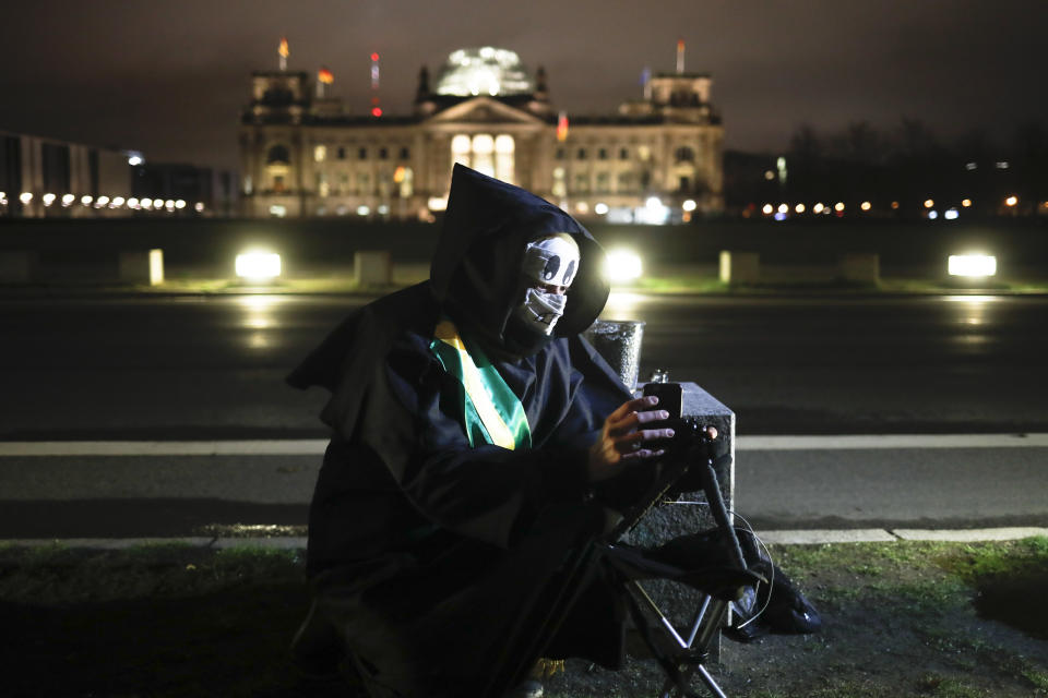 Brazilian activist and artist Rafael Puetter, dressed as the grim reaper, sits in front of the Reichstag and set up a live stream during a one-man protest through Berlin, Germany, early Wednesday, April 7, 2021. The multimedia artist starts his performance at the Brazilian embassy in Berlin at midnight every night to protest against Brazil's COVID-19 policies. Rafael Puetter walks to the Brandenburg Gate and then to the nearby German parliament building, in front of which he counts out a sunflower seed to represent each of the lives that were lost over the past 24 hours in Brazil because of the coronavirus pandemic. (AP Photo/Markus Schreiber)