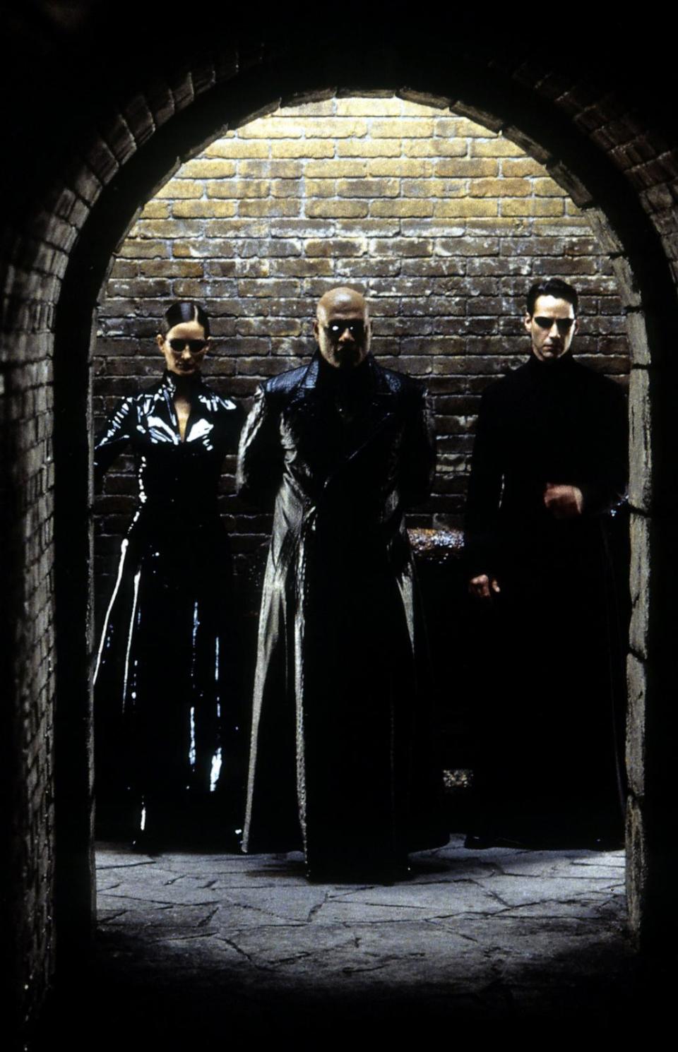 PHOTO: Carrie-Anne Moss, Laurence Fishburne, and Keanu Reeves standing against brick wall in a scene from the film 'The Matrix Reloaded', 2003. (Archive Photos via Getty Images, FILE)
