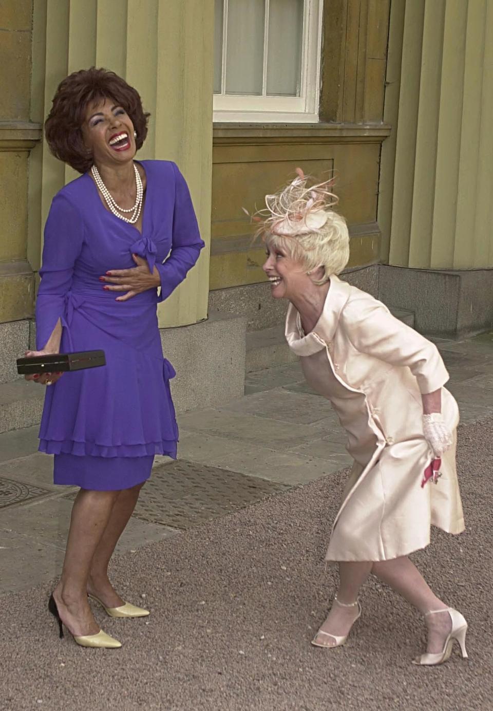 Welsh singer Dame Shirley Bassey is entertained as she receives a curtsy from British actress Barbara Windsor who received an MBE, during a ceremony held at Buckingham Palace where they received their awards from the Queen Elizabeth II. (Photo by John Stillwell - PA Images/PA Images via Getty Images)