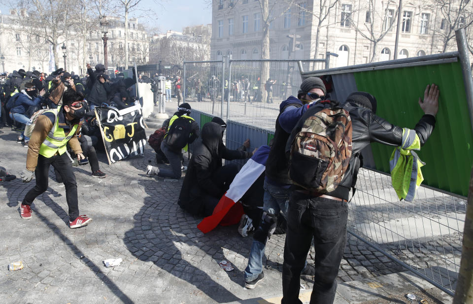 Protesters hide behind street barriers as they clash with police forces during a yellow vests demonstration Saturday, March 16, 2019 in Paris. French yellow vest protesters clashed Saturday with riot police near the Arc de Triomphe as they kicked off their 18th straight weekend of demonstrations against President Emmanuel Macron. (AP Photo/Christophe Ena)