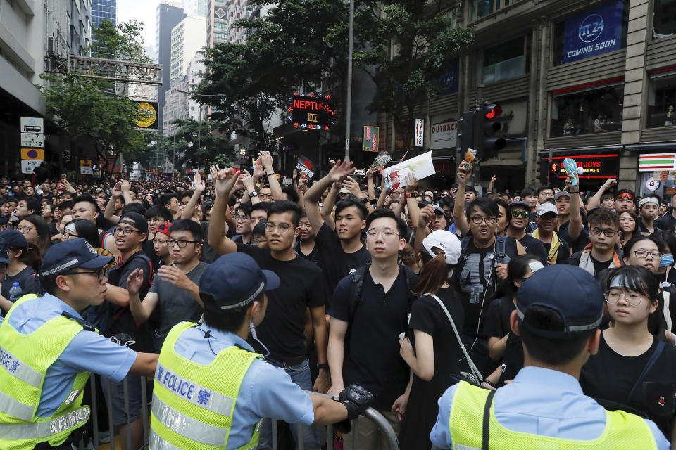 Policemen stand guard behind the barricades as tens of thousands of protesters march through the streets continuing to protest an extradition bill, Sunday, June 16, 2019, in Hong Kong. Hong Kong residents Sunday continued their massive protest over an unpopular extradition bill that has highlighted the territory's apprehension about relations with mainland China, a week after the crisis brought as many as 1 million into the streets. (AP Photo/Kin Cheung)