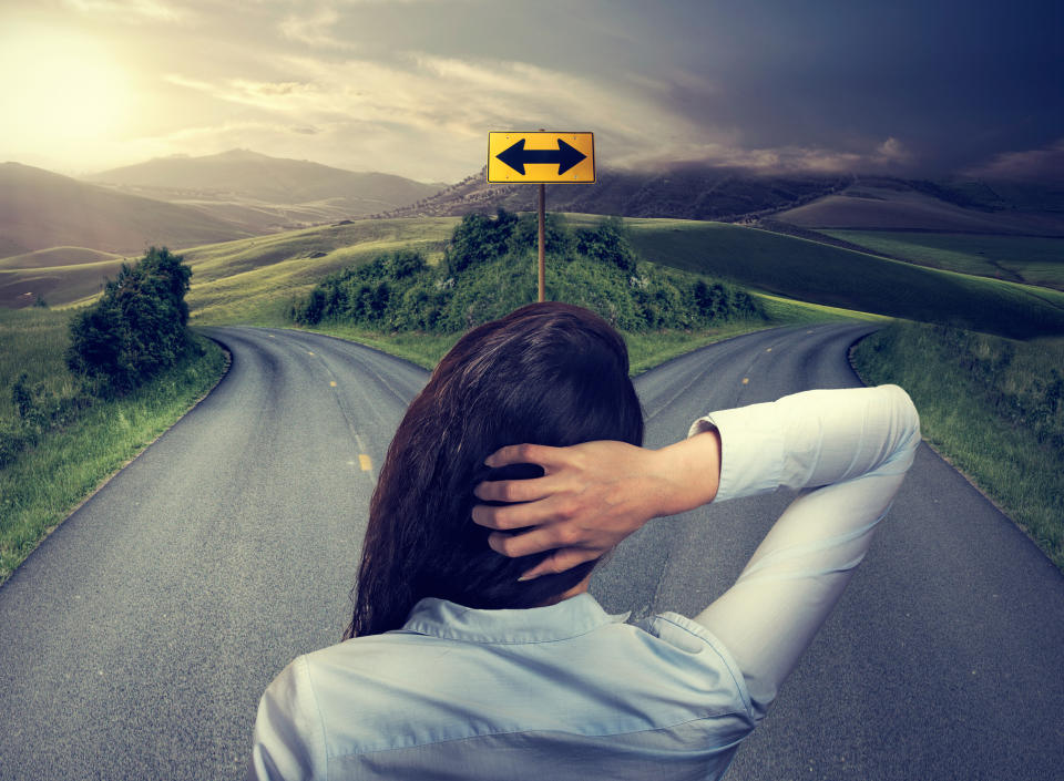 A woman standing at a crossroads with her hand behind her head.