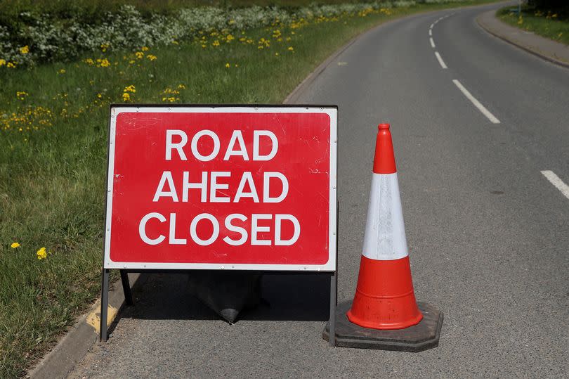A warning sign pointing out the road ahead is closed with a bollard in place blocking traffic