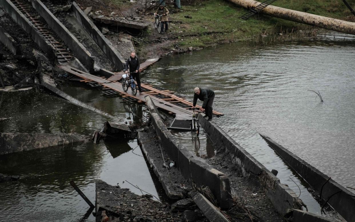 Men cross the destroyed bridge with thier bicycles in the frontline town of Bakhmut in the Donetsk region - YASUYOSHI CHIBA/ AFP