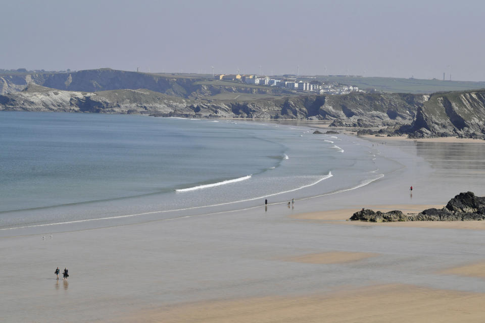 People walk along the normally crowded sands on Tolcarne beach on the north coast of Cornwall, southern England, as the UK continues in lockdown to help curb the spread of the coronavirus, in Newquay, England, Friday April 10, 2020. People are allowed out for personal exercise but public recreation facilities have been closed off due to coronavirus. The highly contagious COVID-19 coronavirus has impacted on nations around the globe, many imposing self isolation and exercising social distancing when people move from their homes. (Ben Birchall / PA via AP)