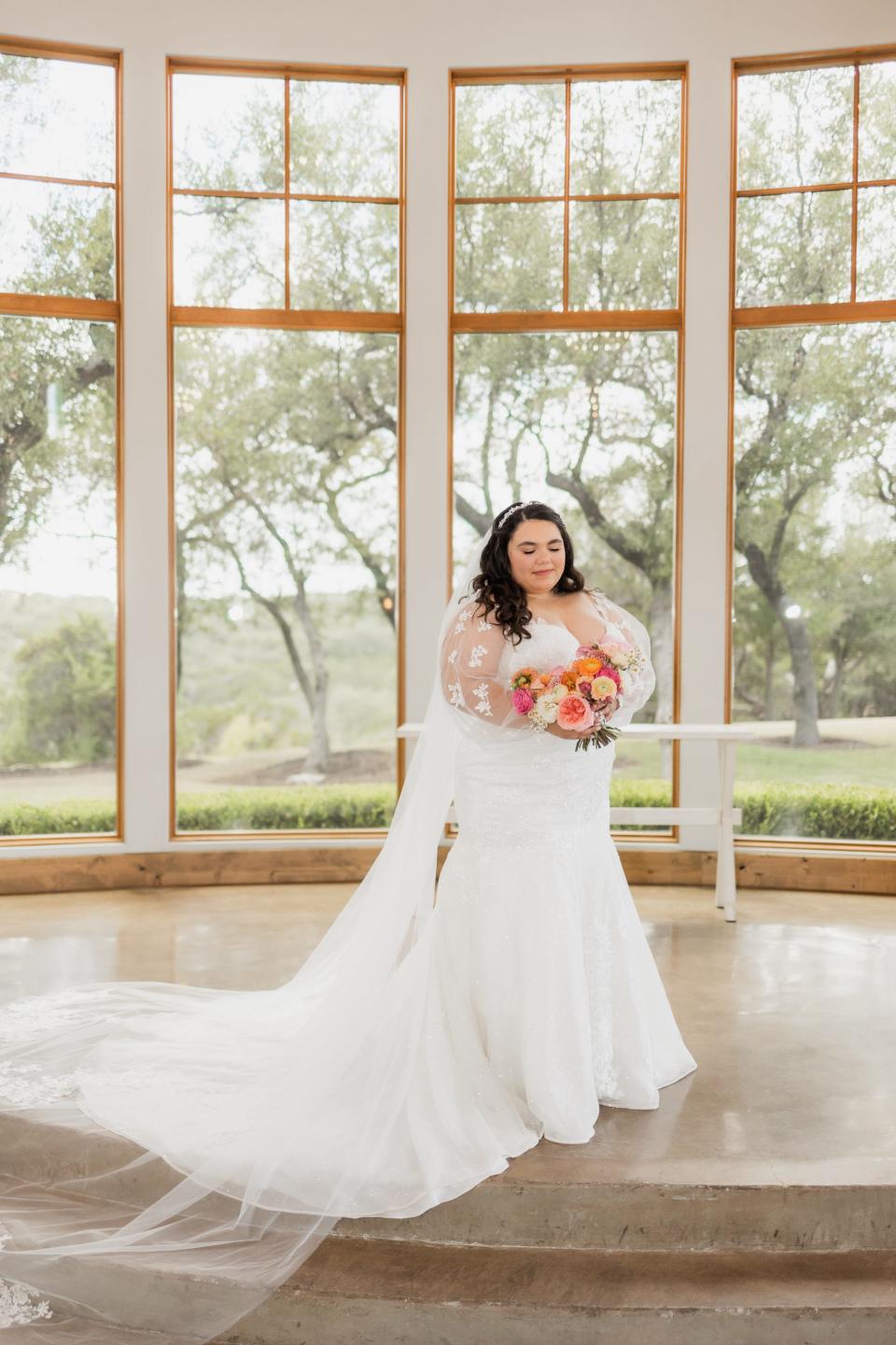 A bride stands in front of a room full of windows.