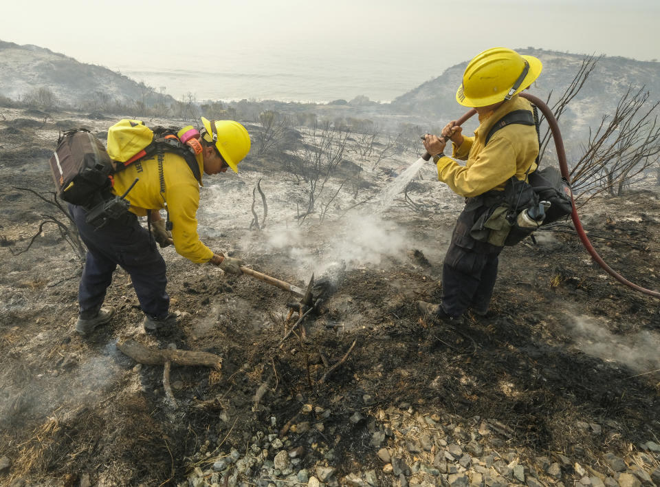 County of Santa Barbara Fire Departement firefighters extinguish a roadside fire off off the U.S. 101 highway Wednesday, Oct. 13, 2021, in Goleta, Calif. A wildfire raging through Southern California coastal mountains threatened ranches and rural homes and kept a major highway shut down Wednesday as the fire-scarred state faced a new round of dry winds that raise risk of flames. (AP Photo/Ringo H.W. Chiu)
