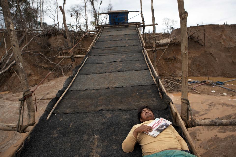 In this May 5, 2014 photo, a miner rests on top of a rustic sluice-like contraption layered with pieces of carpets to capture the gold deposits from water sediment in La Pampa in Peru's Madre de Dios region. Engine noise is the characteristic sound of this Amazonian jungle territory nearly three times the size of Washington DC. There are no trees, only hills of moved earth and artificial ponds of brown water where gold is mined. (AP Photo/Rodrigo Abd)