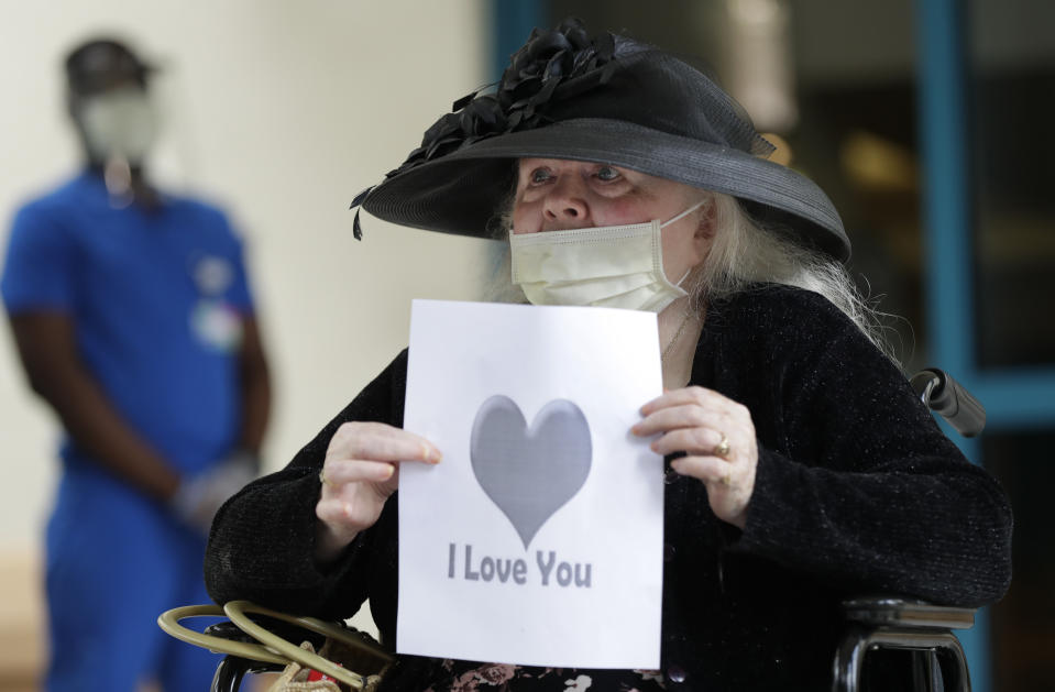 Margaret Choinacki, 87, who has no other family members left because her husband and daughter have died, holds up a sign as her friend Frances Reaves drives-by for a visit, Friday, July 17, 2020, at Miami Jewish Health in Miami. Miami Jewish Health has connected more than 5,000 video calls and allowed drive-by visits where friends and family emerge through sunroofs to see their loved ones. (AP Photo/Wilfredo Lee)