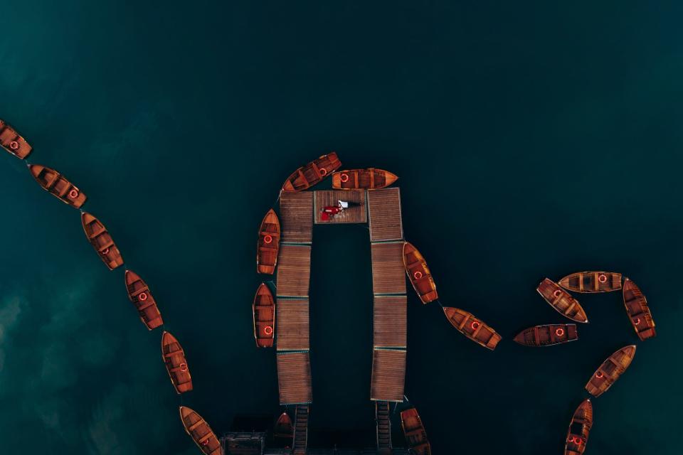 A couple lies on a boardwalk surrounded by colorful boats in an aerial shot.