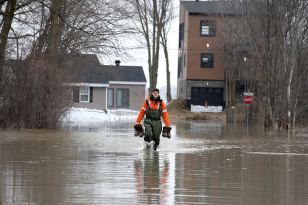 A resident carries his boots as he walks on the flooded street in front of his home in Rigaud, Quebec, Canada April 21, 2019. REUTERS/Christinne Muschi