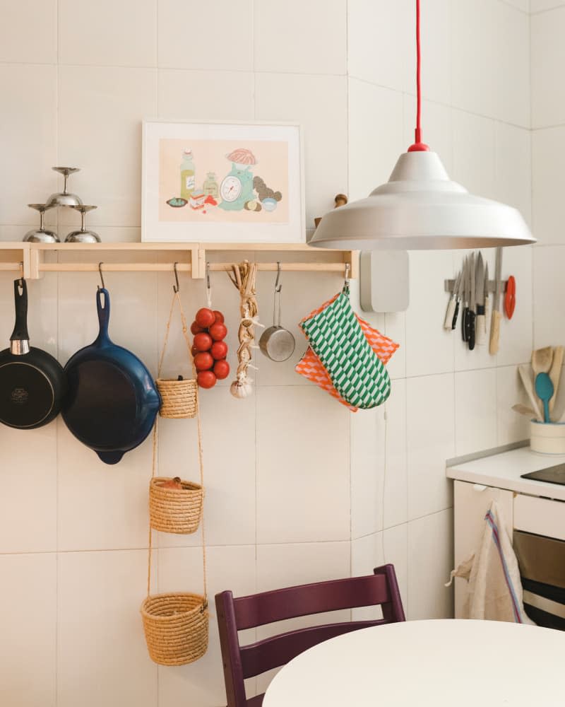 White tile kitchen with pots and pans and other tools hanging from wood floating shelf