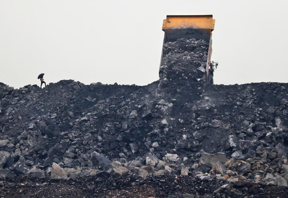 In this Oct. 23, 2019, photo, a laborer keeps watch as coal is unloaded from a truck in the village of Rajapur in Jharia, a remote corner of eastern Jharkhand state, India. The fires started in coal pits in eastern India in 1916. More than a century later, they are still spewing flames and clouds of poisonous fumes into the air, forcing residents to brave sizzling temperatures, deadly sinkholes and toxic gases. (AP Photo/Aijaz Rahi)