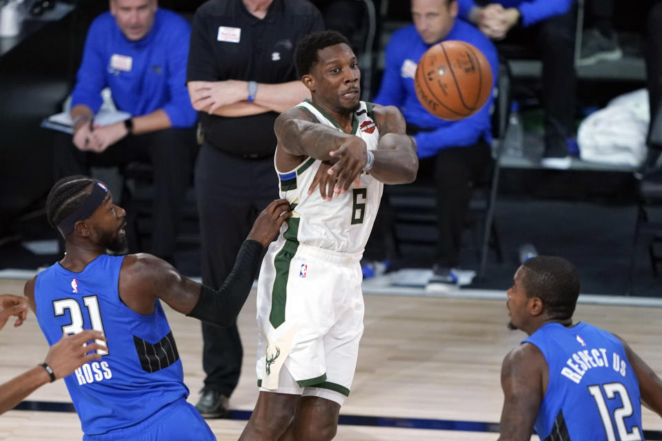 Milwaukee Bucks' Eric Bledsoe (6) passes the ball between Orlando Magic's Terrence Ross (31) and Gary Clark (12) during the first half of an NBA basketball first round playoff game Saturday, Aug. 29, 2020, in Lake Buena Vista, Fla. (AP Photo/Ashley Landis)