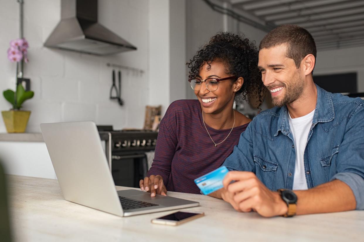 Smiling young couple shopping online with credit card and laptop at home