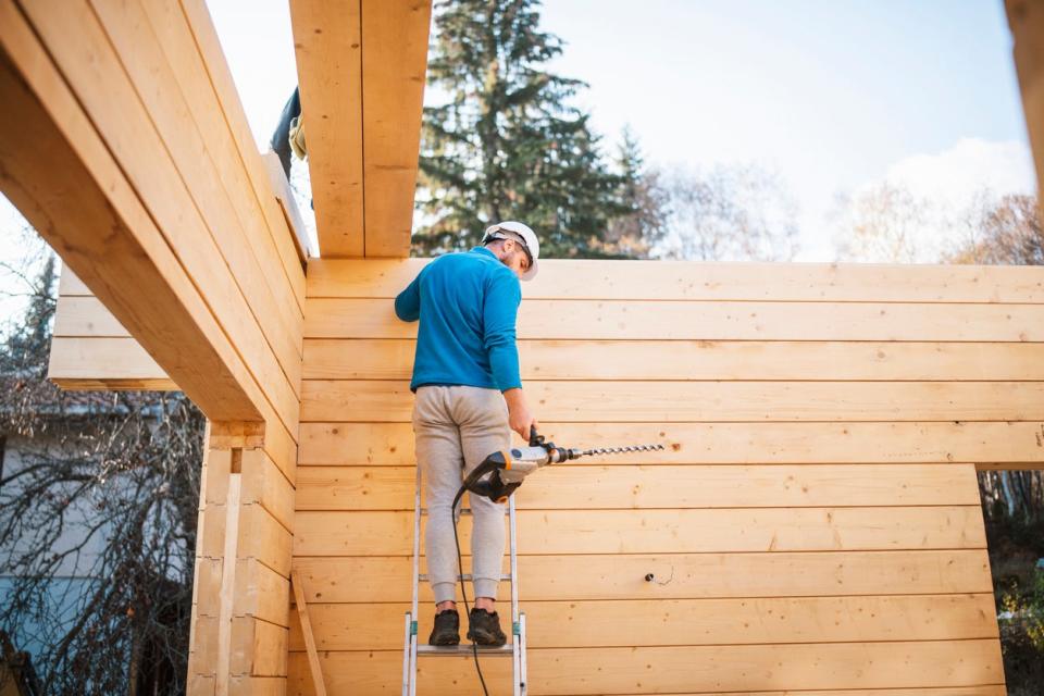 A person in a teal shirt stands on a ladder during a building project.