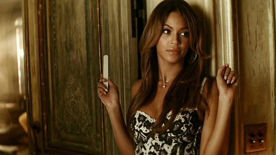 Beyonce stands holding a nail file, looking off-screen, in a house