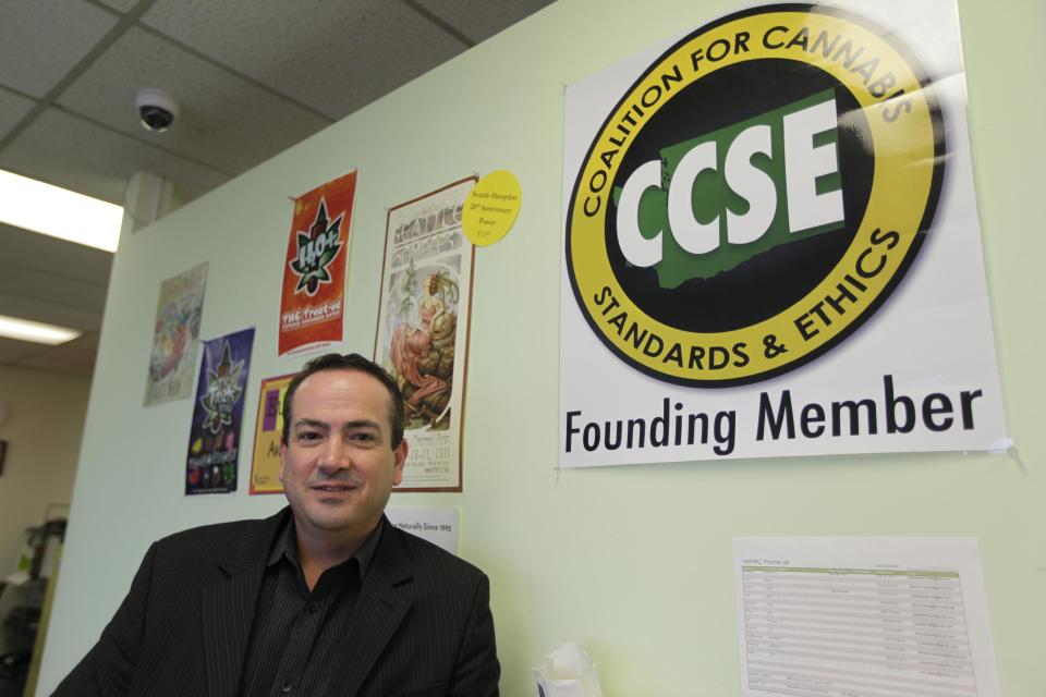 John Davis, chairman of the Coalition for Cannabis Standards and Ethics self-regulating trade organization, and co-owner of the Northwest Patient Resource Center medical marijuana dispensary, poses for a photo next to the CCSE certification logo, Wednesday, Nov. 7, 2012, at his dispensary in Seattle. After voters weighed in on election day, Colorado and Washington became the first states to allow pot for recreational use, but they are likely to face resistance from federal drug warriors. Davis, who says it would make sense for his business to evolve from serving medical patients to the general public, says that the CCSE has offered to work with Washington state regulators to help them develop policy and legal guidelines relating to the legal use of marijuana. (AP Photo/Ted S. Warren)