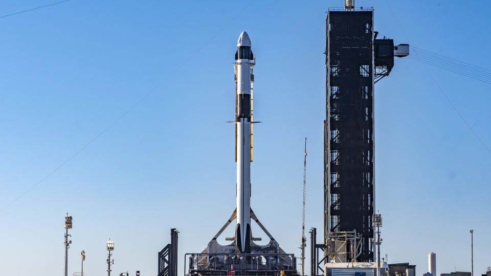 A white and black SpaceX Falcon 9 rocket sits on its launch pad before launch.