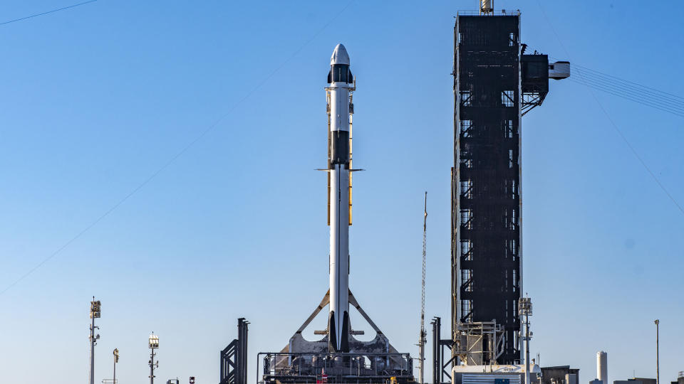 A white and black SpaceX Falcon 9 rocket stands on its launch pad before launch.