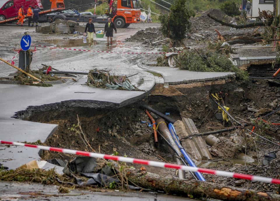 People carry their belongings past a broken road in Schuld, Germany, Friday, July 16, 2021. Two days before the Ahr river went over the banks after strong rain falls causing severals deaths and hundreds of people missing. (AP Photo/Michael Probst)