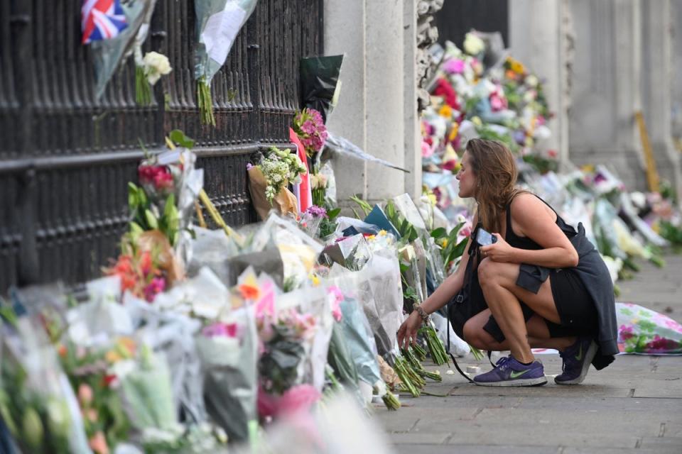 A woman places flowers at Buckingham Palace, following the passing of Britain's Queen Elizabeth (REUTERS)