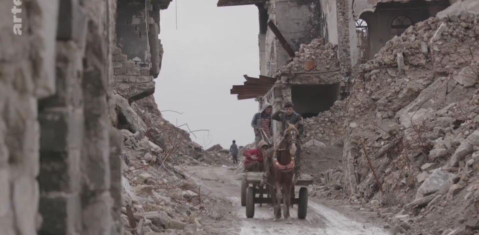 Jungs fahren auf einem Pferde-Anhänger durch Trümmerschluchten. Vielerorts ist Mossul noch vollständig zerstört. Foto: Screenshot / ARTE