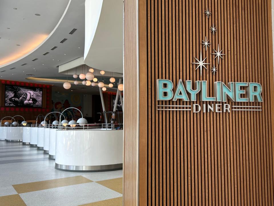 The sign for the Bayliner Diner. The word Bayliner is in teal. Behind the sign is a retro diner with checkerboard flooring.